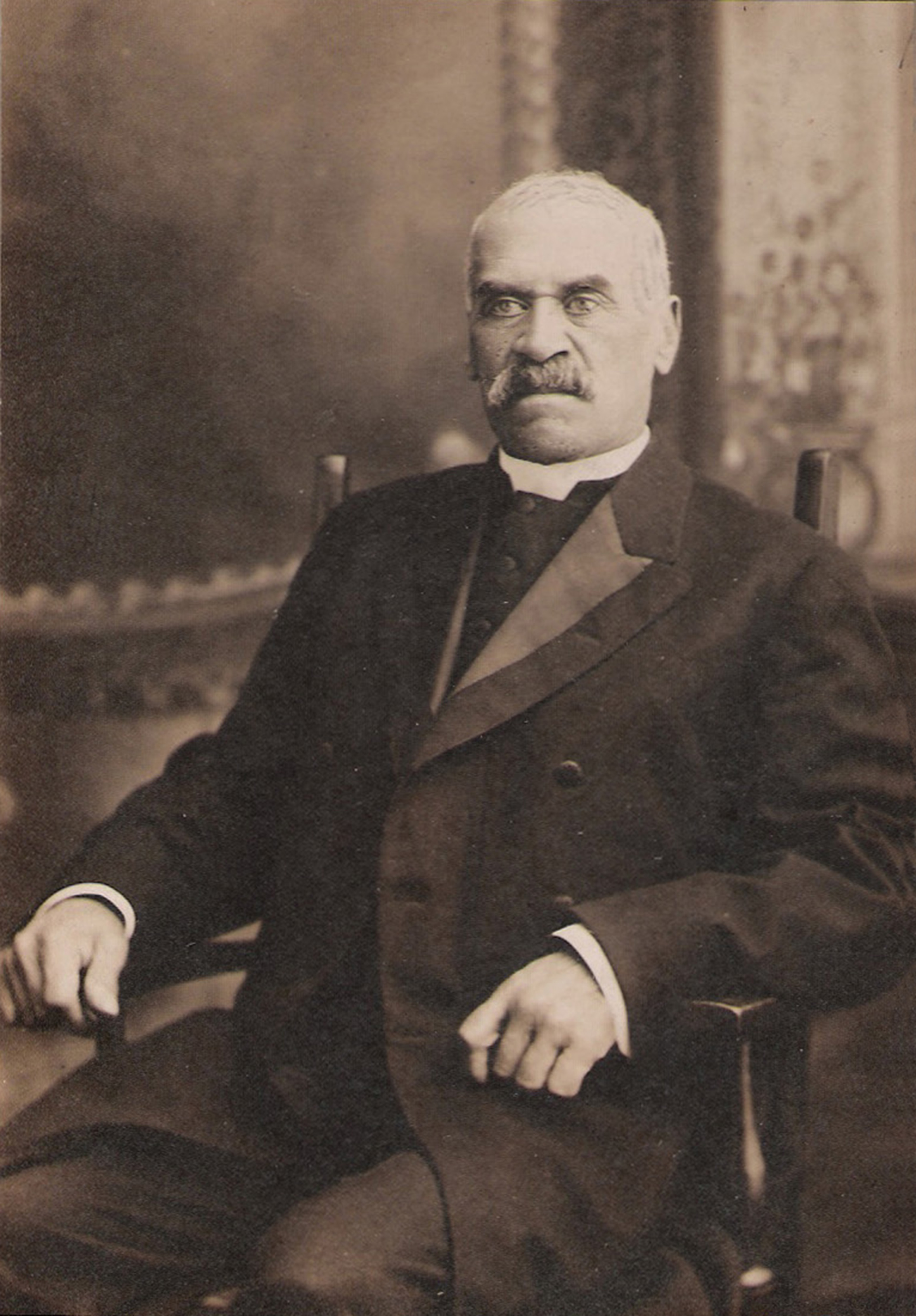 Portrait of Rev. Ball. He is seated in a chair and wearing a dark coloured suit.